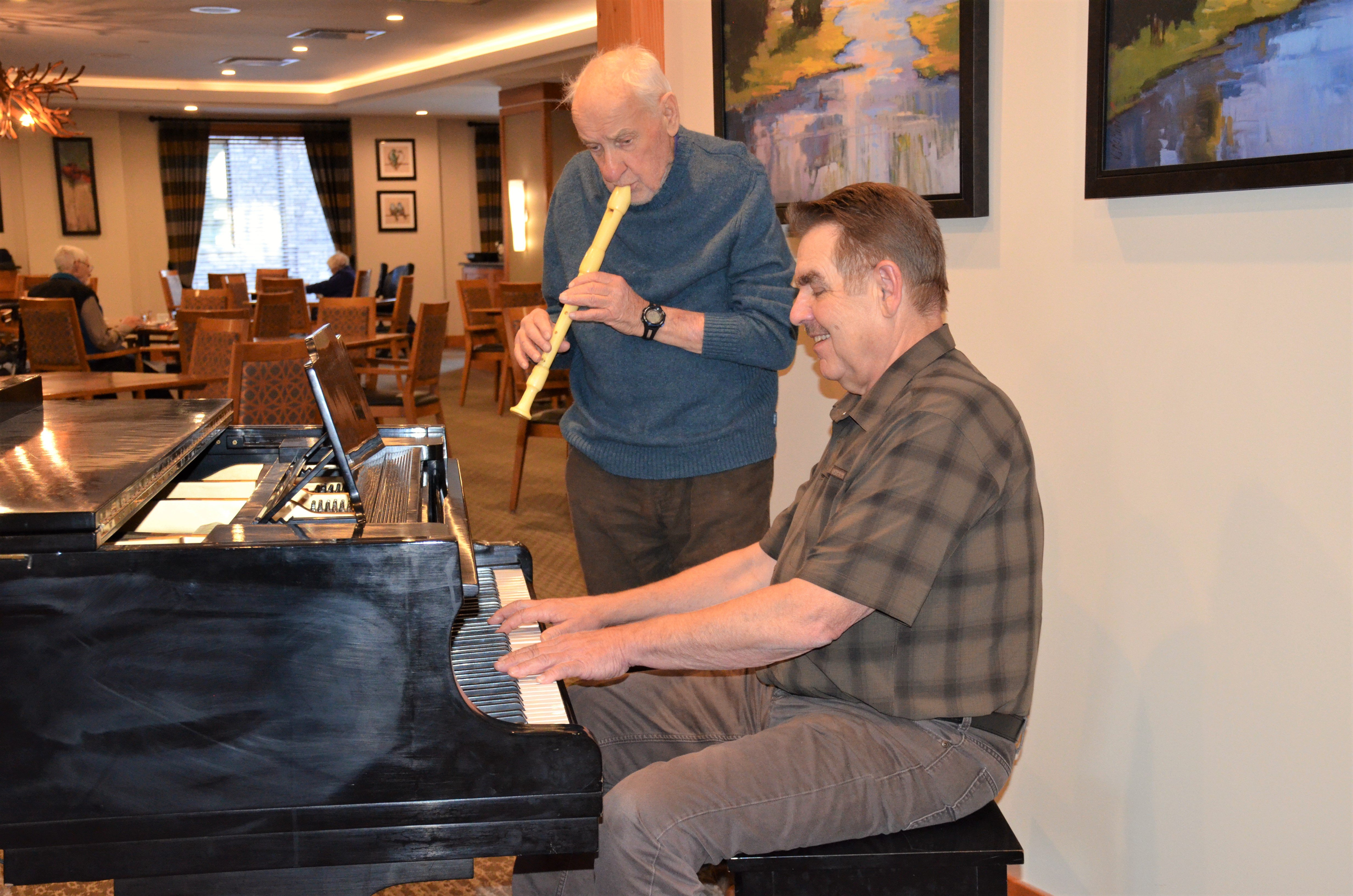 Ken playing a recorder along with Rick playing the piano together in a beautiful dining room