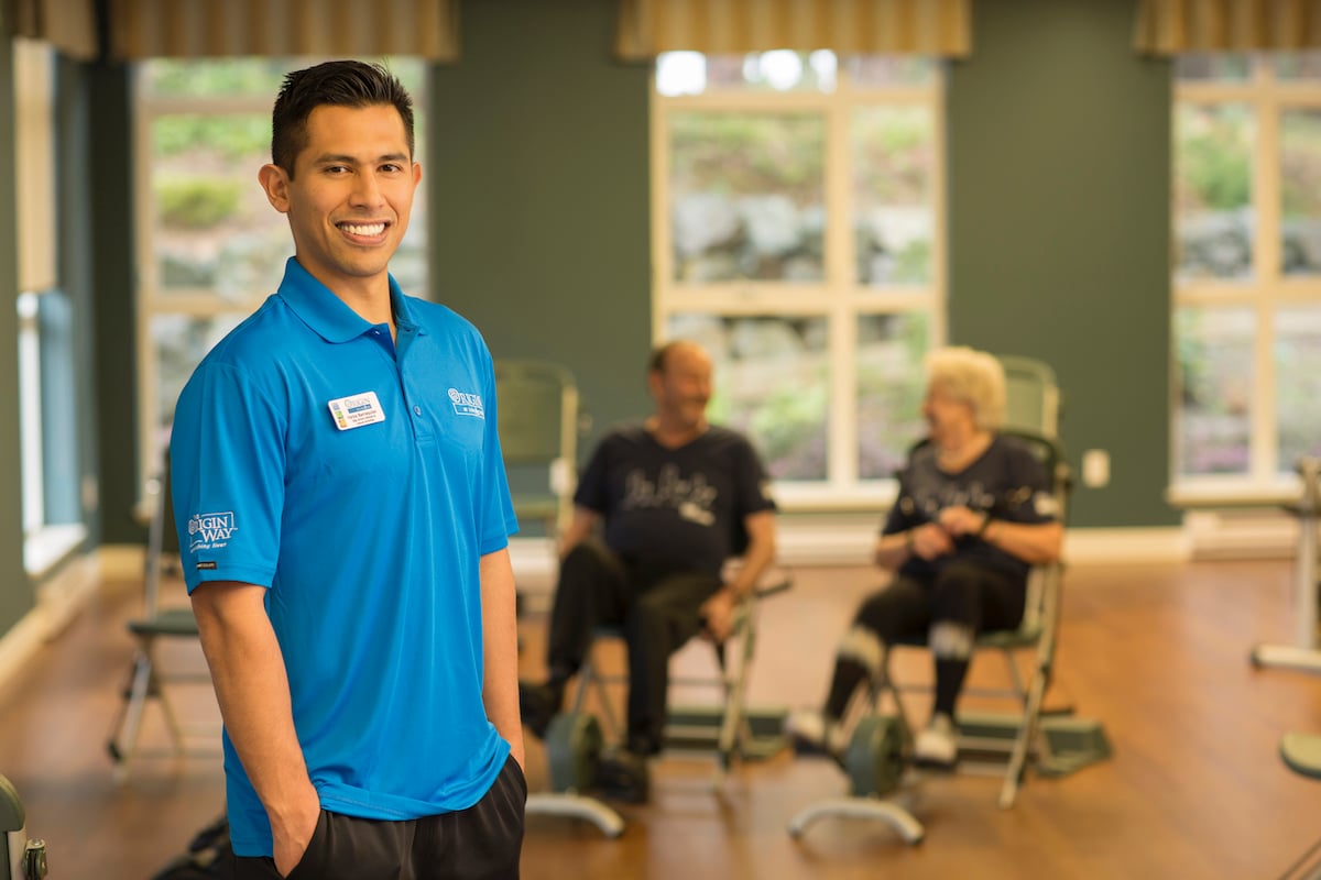 Faress standing in the movement studio with 2 residents in the background exercising